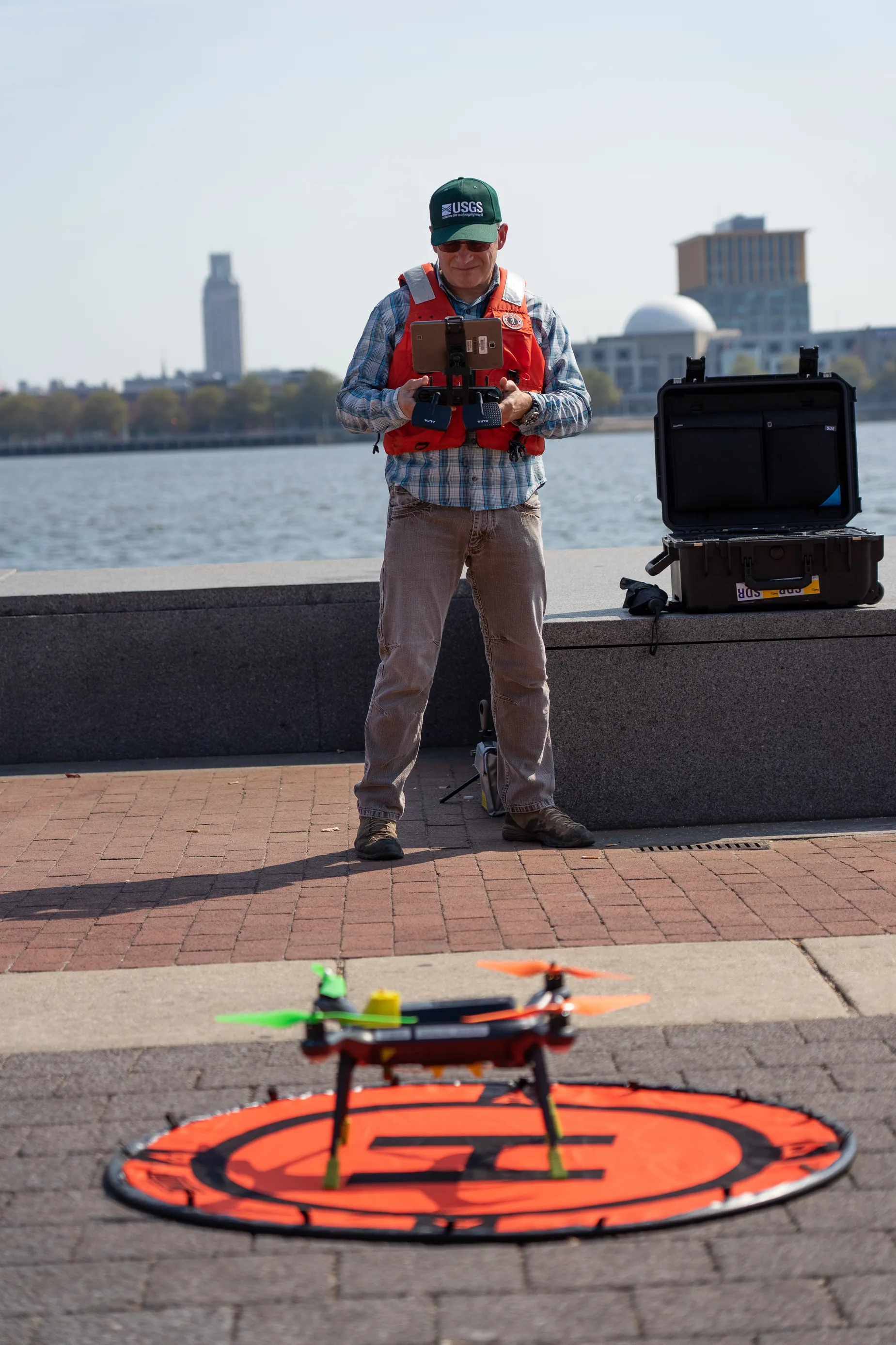 USGS operator holds a controller behind a small drone on a landing pad beside a river