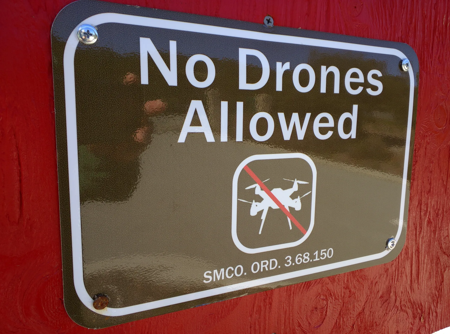 A No Drones Allowed sign on red wood, with a crossed-out quadcopter and a San Mateo County ordinance reference