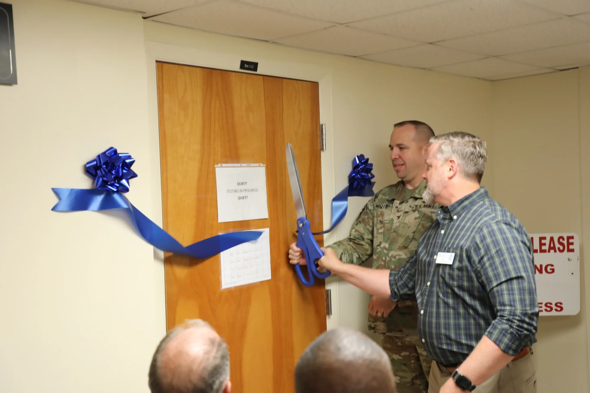 Two officials cut a blue ribbon outside a testing room at the Fort Novosel Education Center.